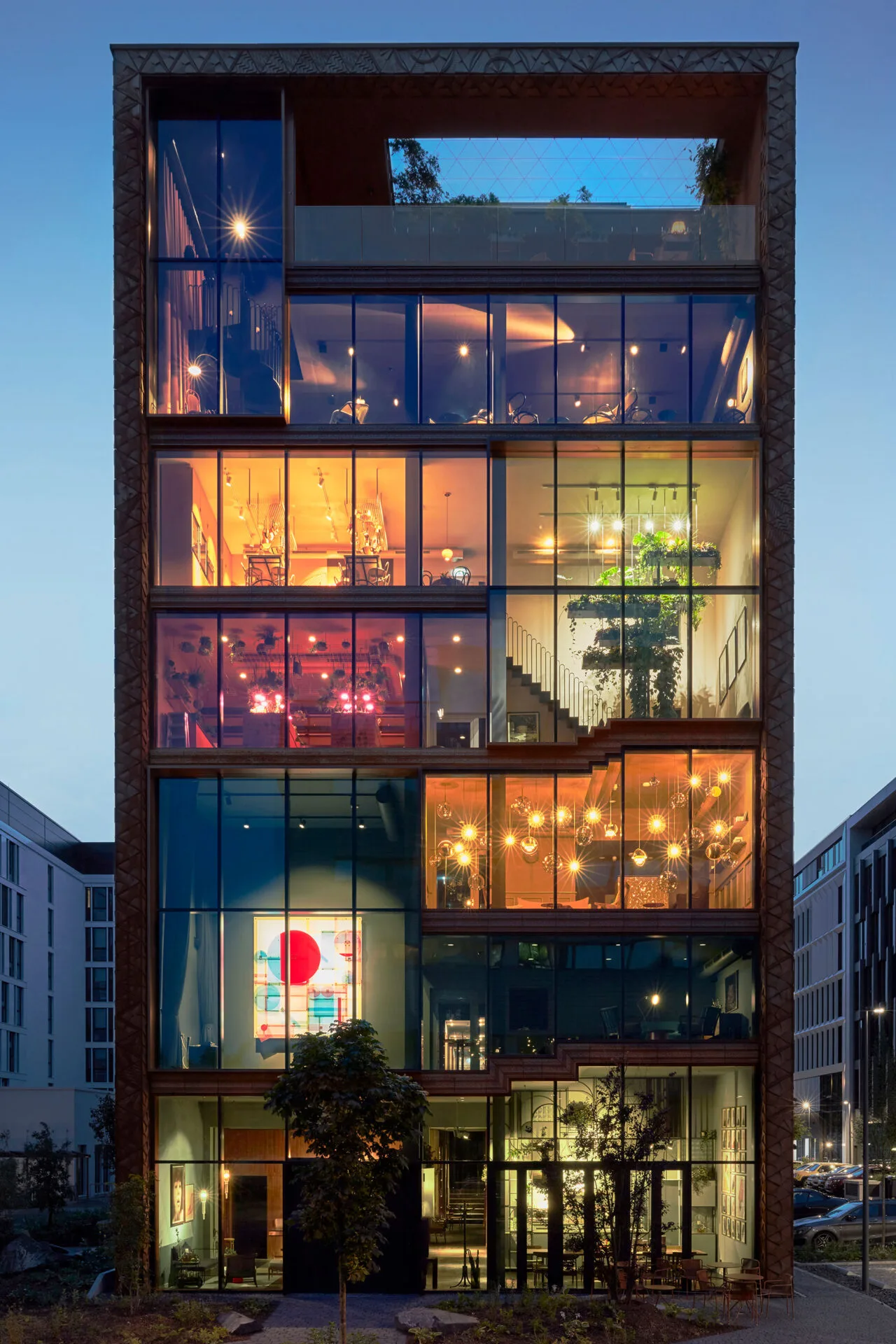 Fassade des Lindley Lindenberg Hotels in Frankfurt mit sichtbaren Innenräumen und warmem Licht bei Dämmerung.