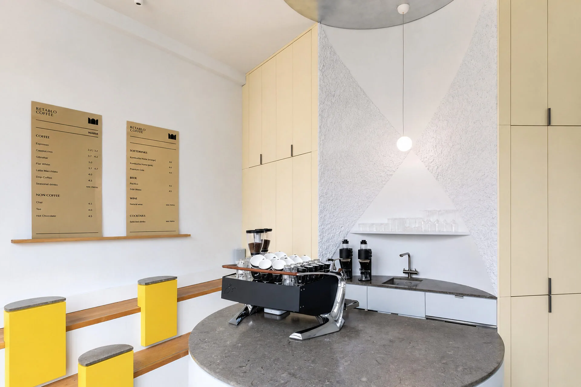 Retablo Coffee Bar mit Espressomaschine, runder Naturstein-Theke und gelben Einbauten