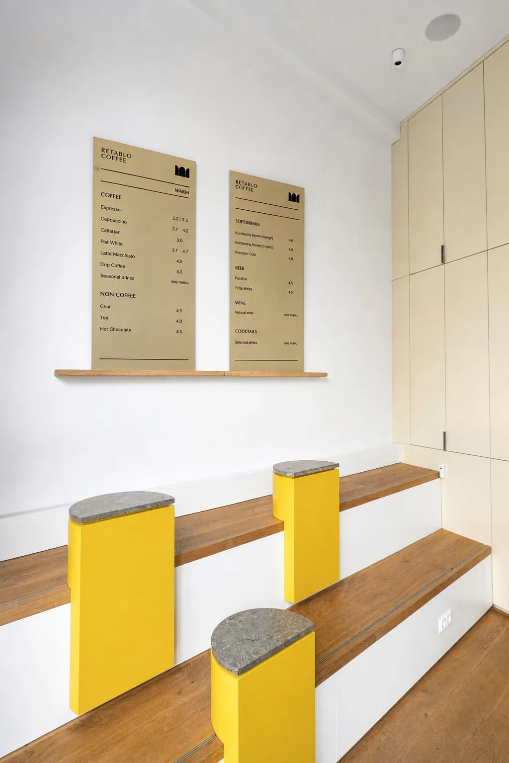 Retablo Coffee Innenraum mit Menutafeln, gelben Hockern und Holz-Sitzstufen.