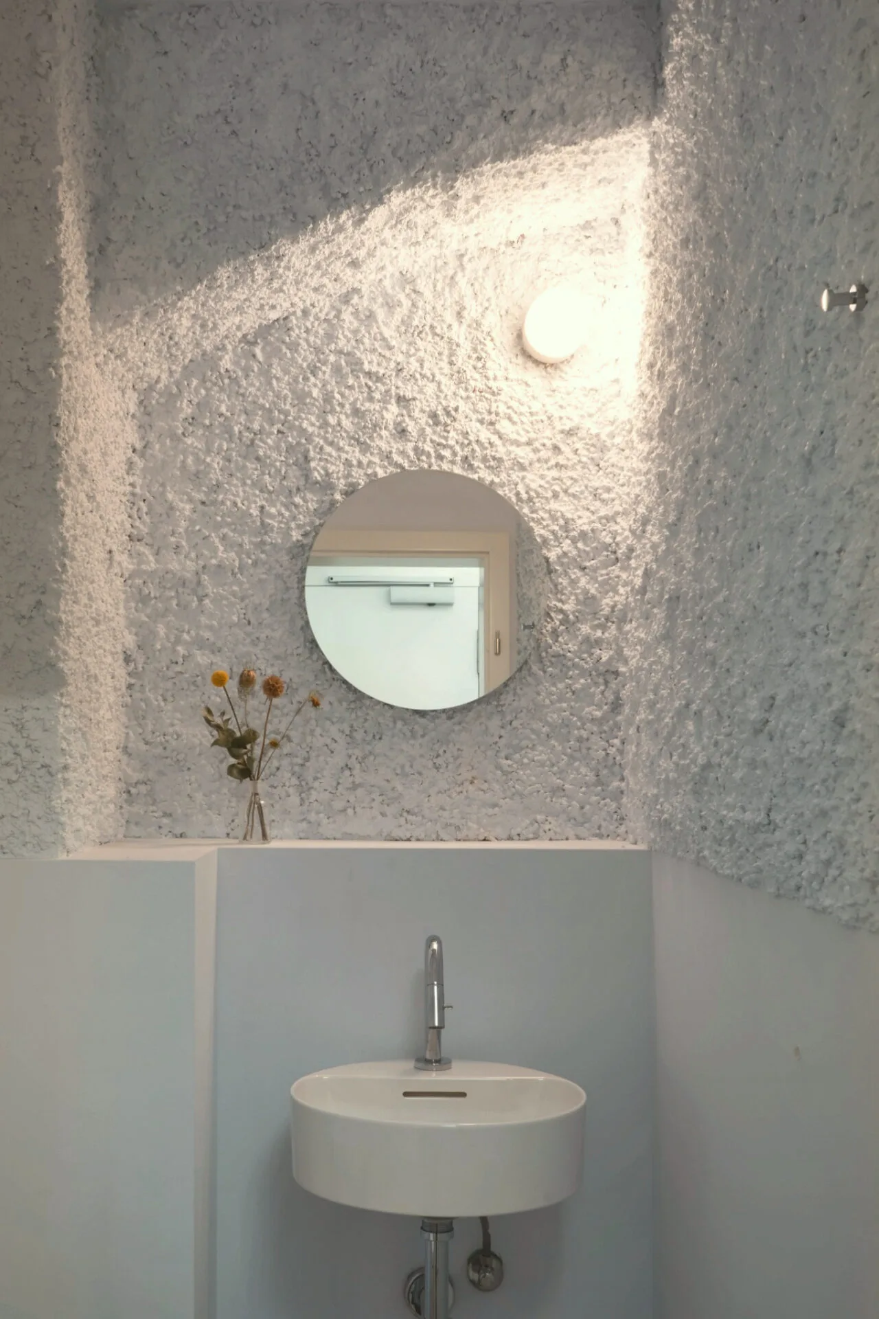 Waschbereich im Retablo Coffee mit weißer Strukturwand, Rundspiegel und Wandlicht.